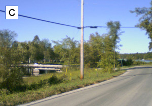 Waypoint C: looking along the road toward a low bridge over the water on the left, with a hydro pole in the foreground.
